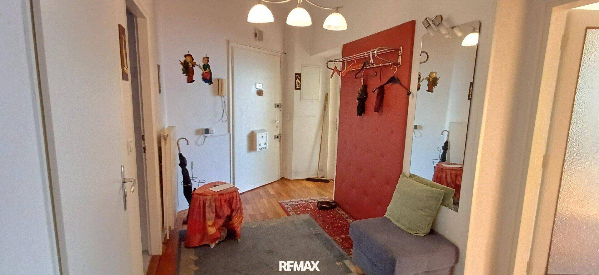 Eingangsbereich mit roter Wandverkleidung, Spiegel, Garderobe und Zugang zu weiteren Räumen.
