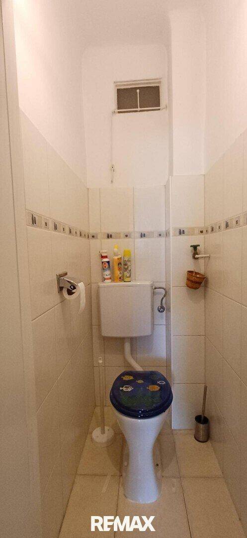 Kleines WC mit Toilette, Fliesenwänden und einem kleinen Fenster für Belüftung.