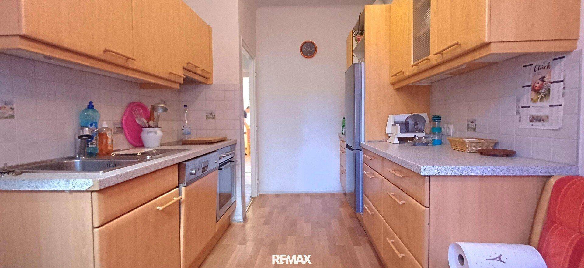 Schmale Küche mit hellen Holzschränken, Spüle, Geschirrspüler und Kühlschrank in funktionalem Design.