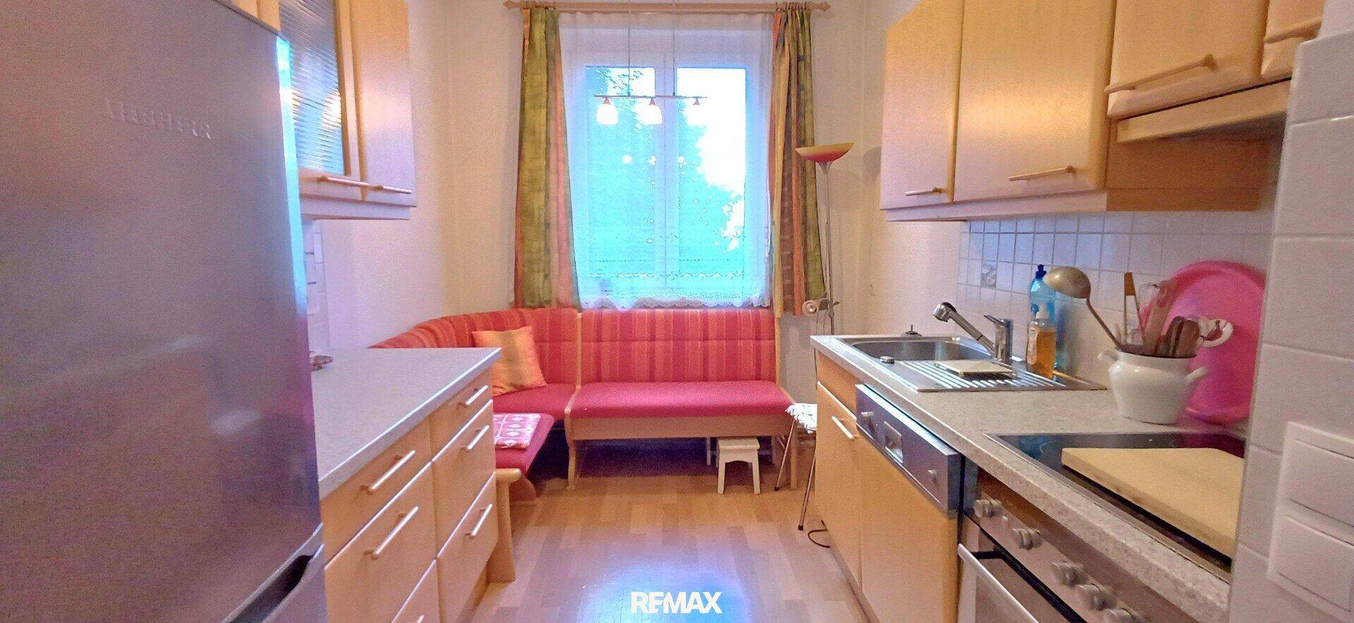 Gemütliche Küche mit Holzschränken, Einbauküche, Kühlschrank und einer roten Sitzecke am Fenster.