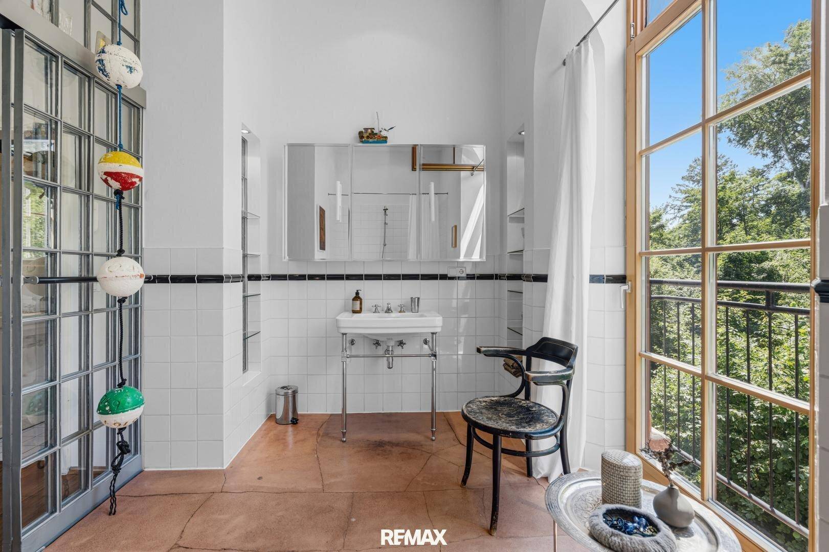 Badezimmer mit Waschbecken, Spiegel und großem Fenster, das viel Tageslicht hereinlässt.