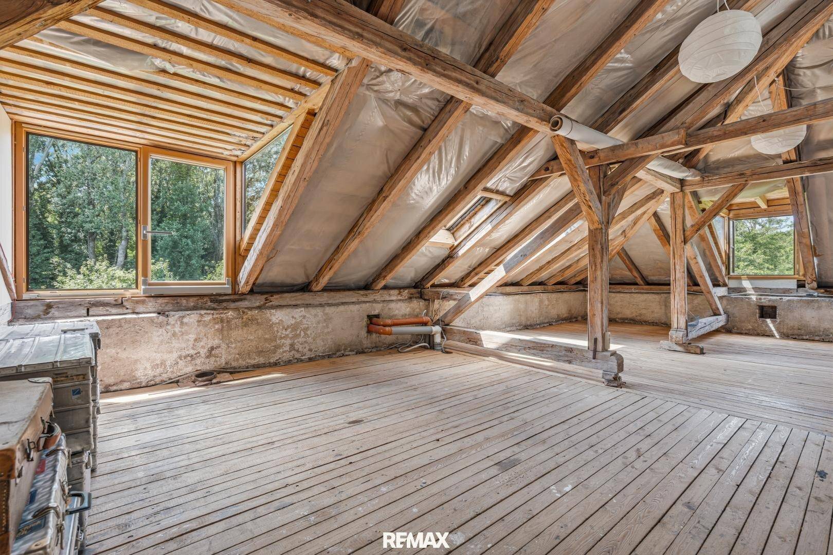 Geräumiger Dachboden mit Holzboden, sichtbaren Dachbalken und Fenstern.