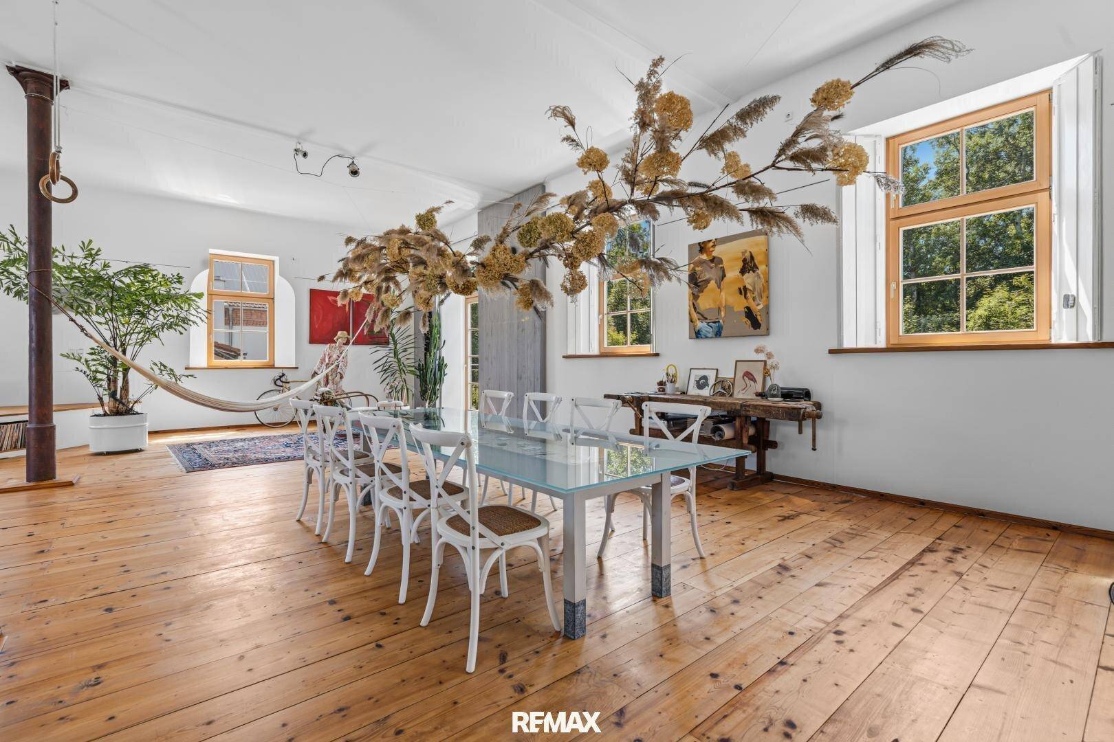 Eleganter Essbereich mit großem Glastisch, Holzboden und hohen Fenstern.