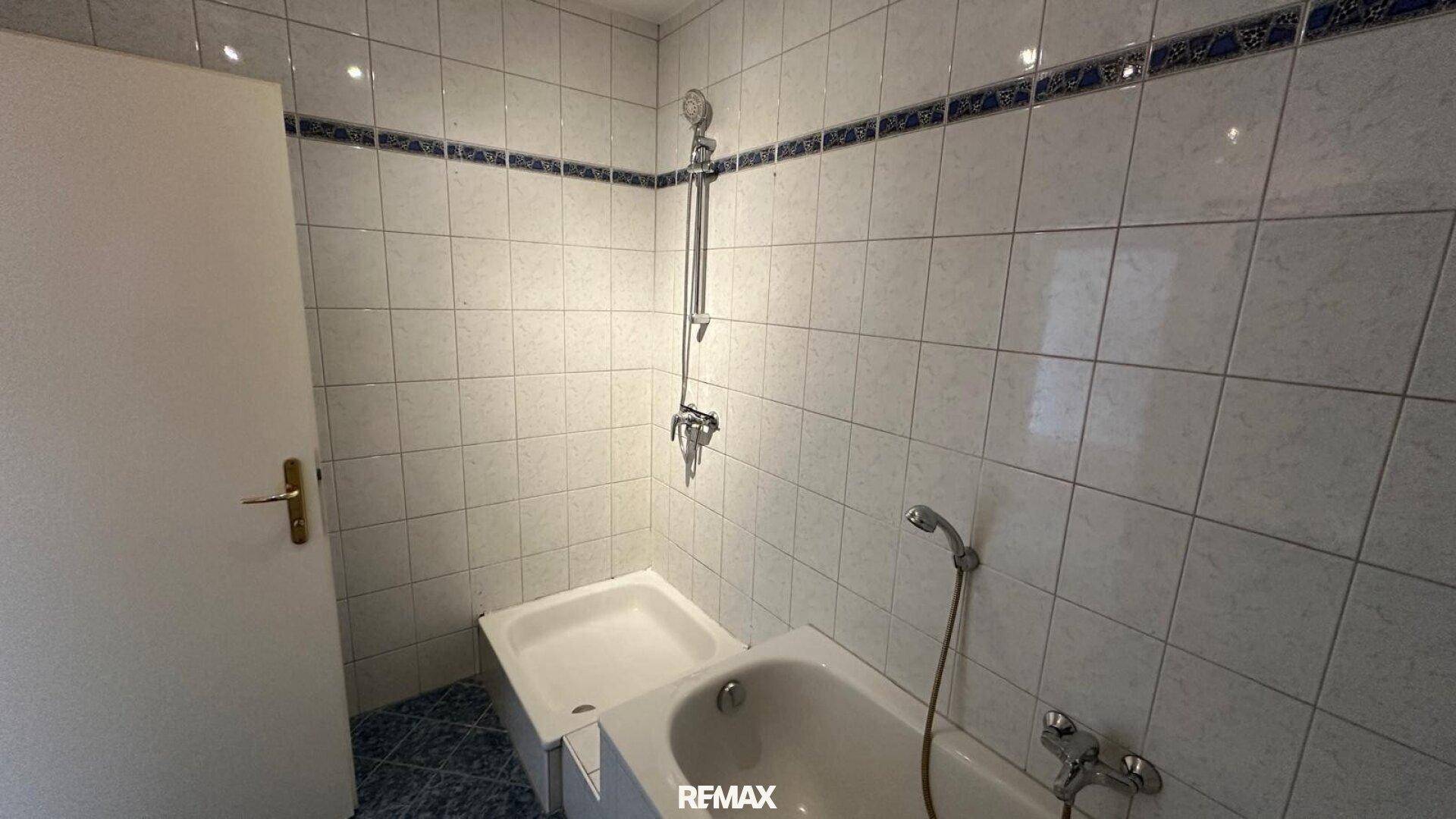 Klassisches Badezimmer mit Badewanne, Duschvorrichtung und weiß-blauen Fliesen.