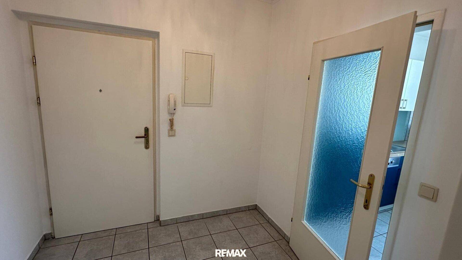 Heller Flur mit Fliesenboden, einer weißen Tür und einer Glastür zu einem weiteren Raum.