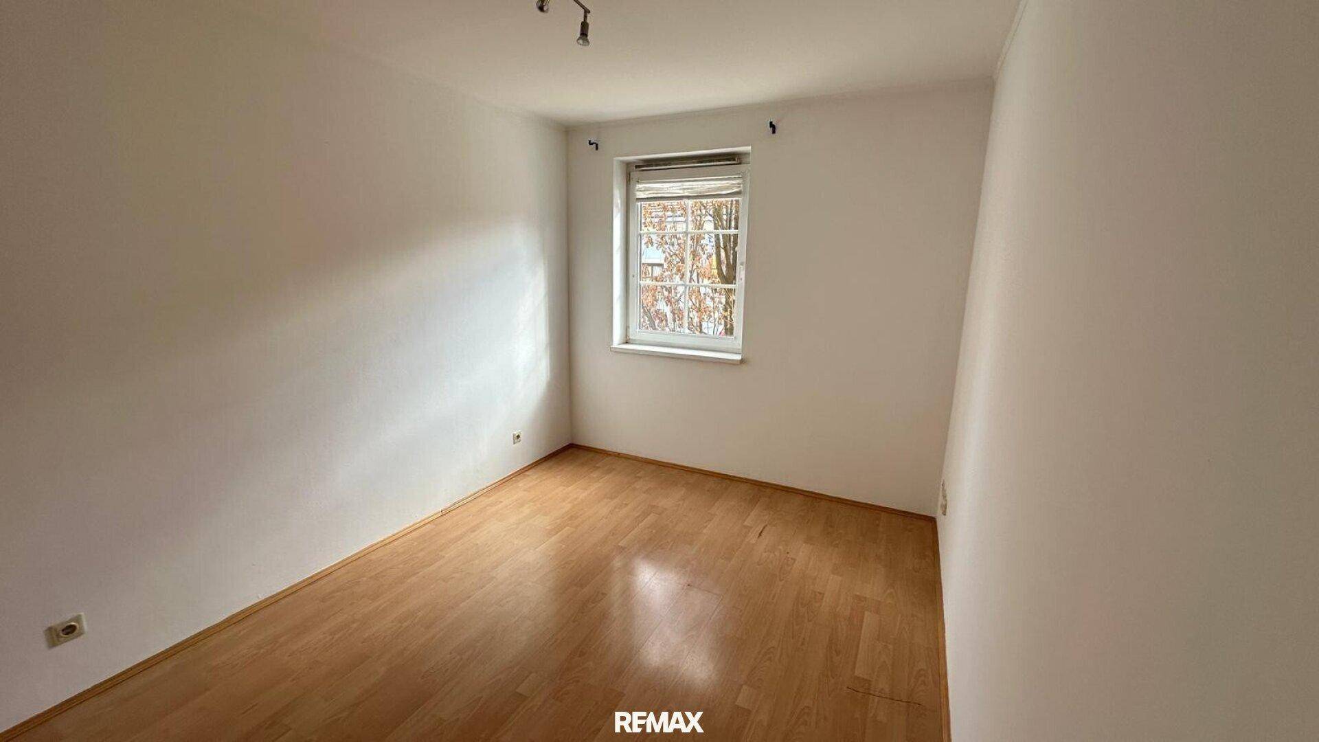 Ruhiges Schlafzimmer mit hellem Parkettboden und einem Fenster für natürliches Licht.