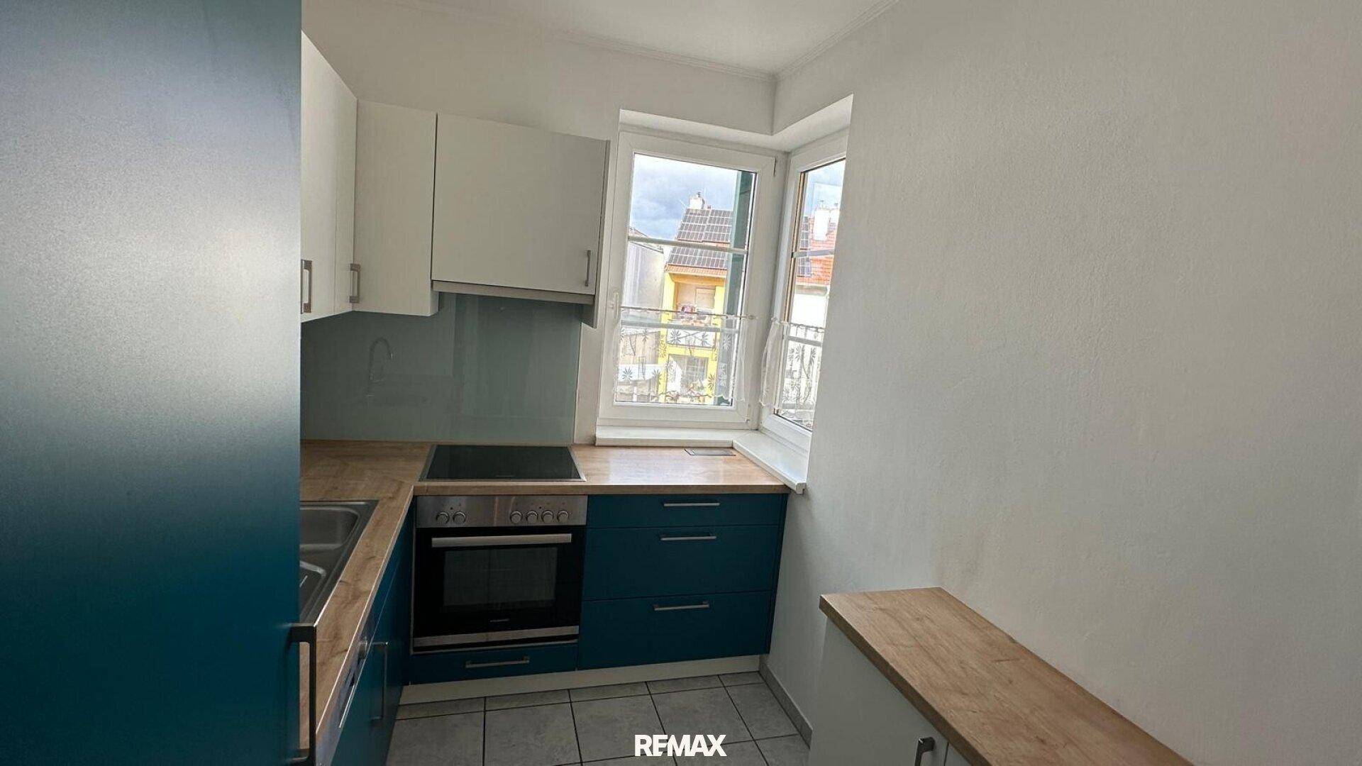 Funktionale Küche mit blauen Unterschränken, weißen Oberschränken und Holz-Arbeitsplatte.