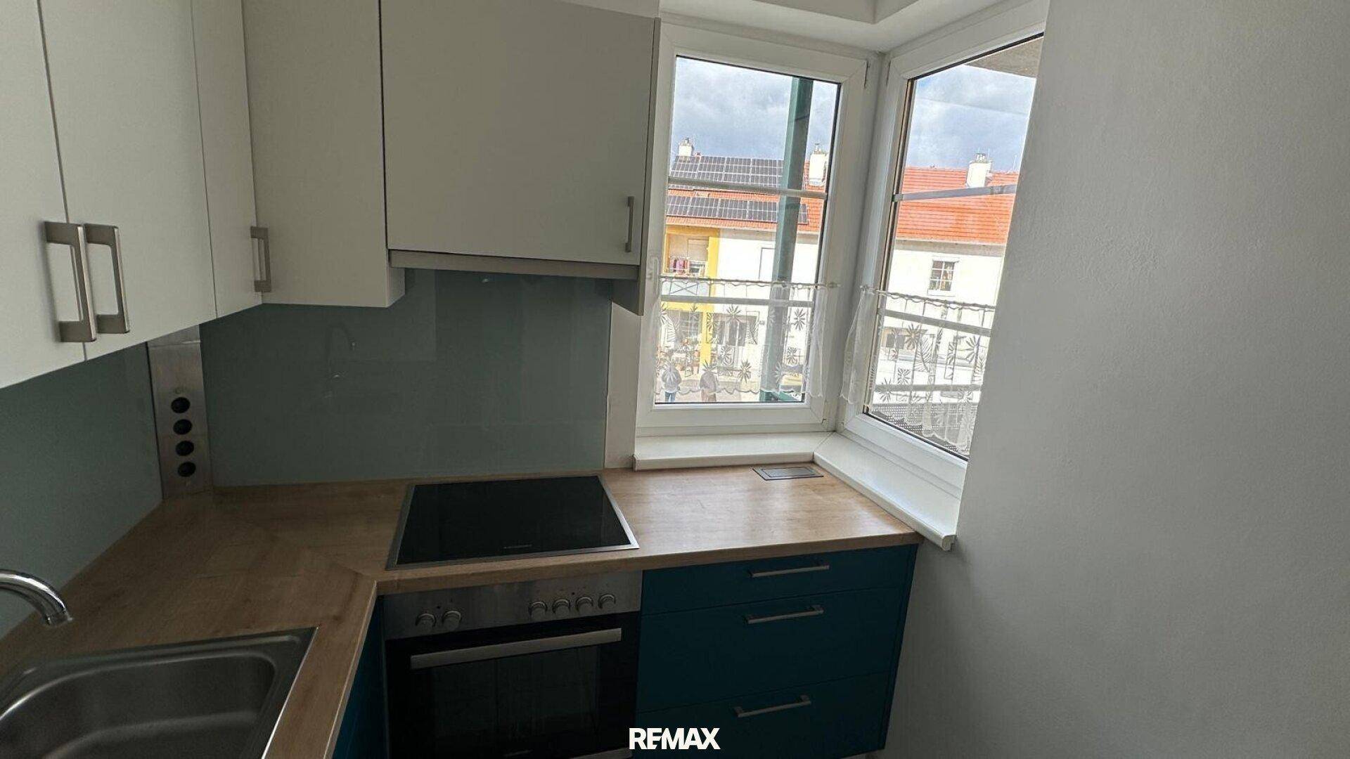 Moderne Einbauküche mit blauen und weißen Schränken, Holz-Arbeitsplatte und Fenster.