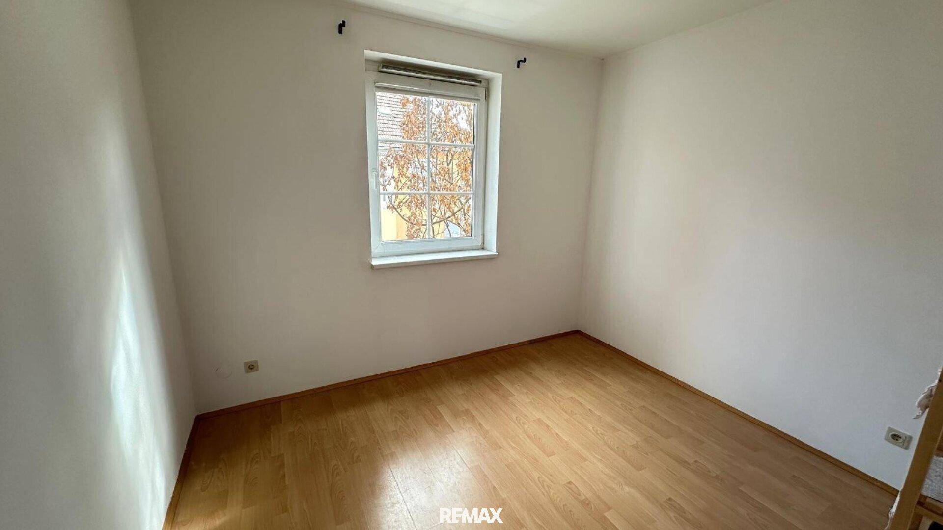 Gemütliches Schlafzimmer mit hellem Parkettboden und einem Fenster, das Tageslicht hereinlässt.