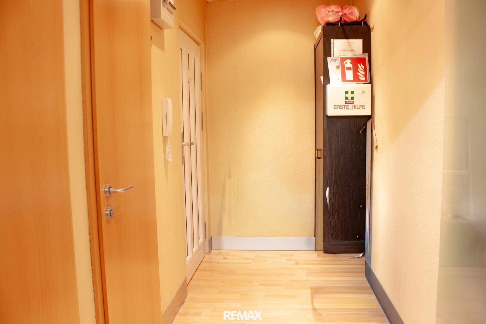 Schmaler Flur mit hellem Holzboden, gelben Wänden und einem Schrank mit Sicherheitsausrüstung.