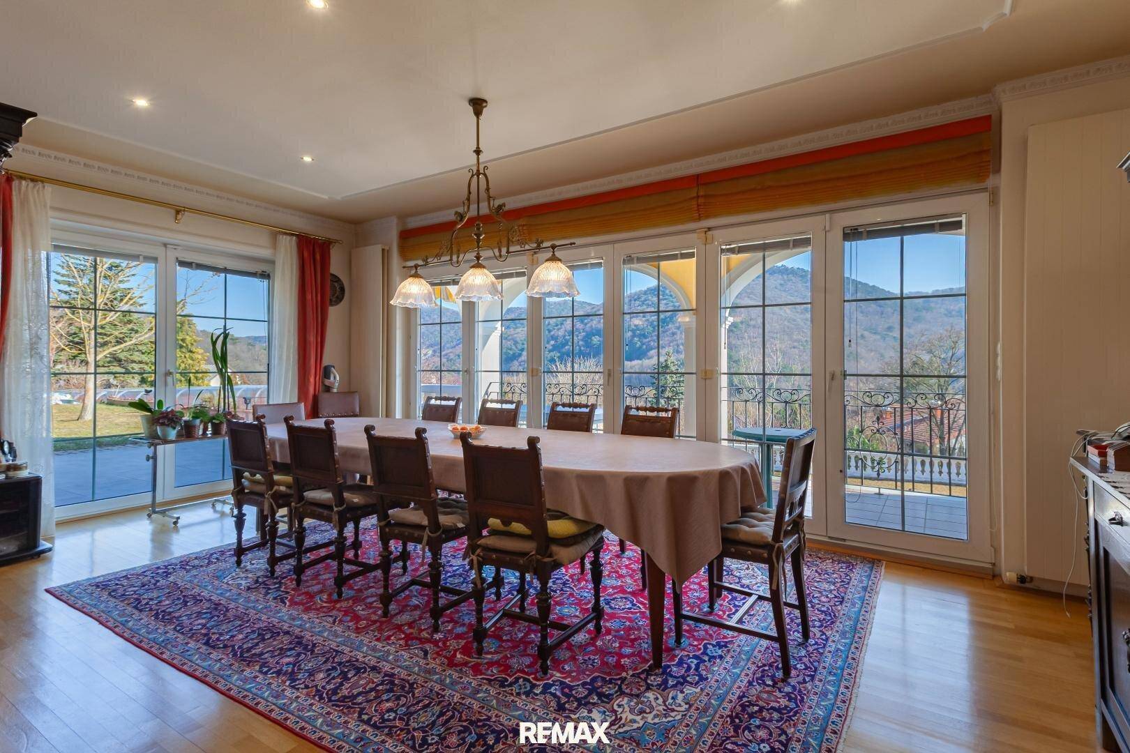 Elegantes Esszimmer mit großem Holztisch, Parkettboden und Zugang zur Terrasse mit Bergblick.