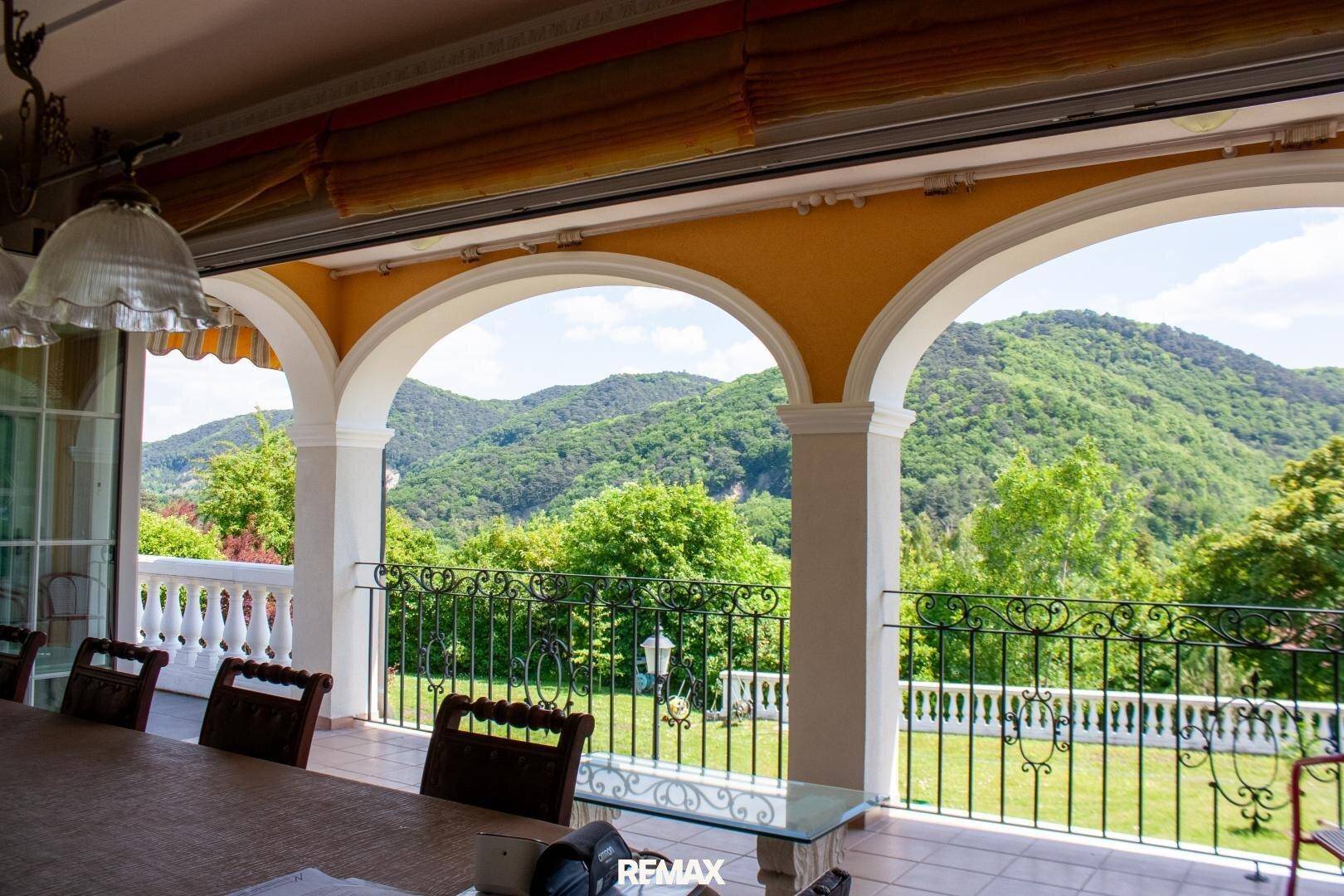 Überdachte Loggia mit Bögen und schmiedeeisernem Geländer bietet einen weiten Blick auf die grünen Berge.