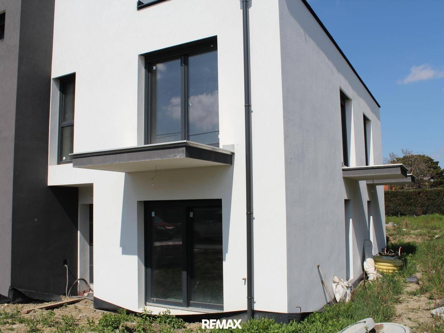 Nahaufnahme der modernen weißen Fassade mit dunklen Fensterrahmen und einem kleinen Balkonüberstand.
