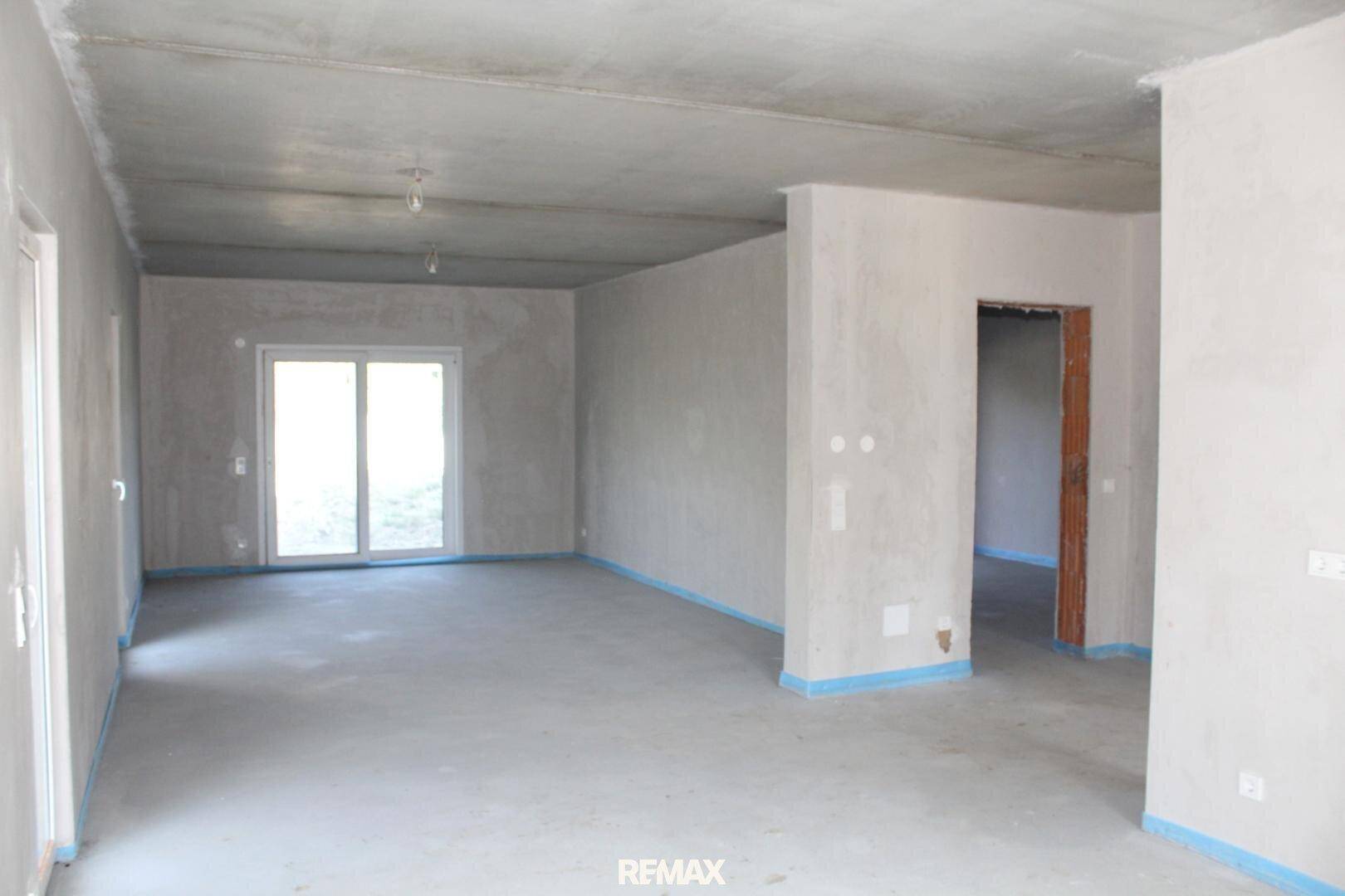 Unfertiger Wohnbereich im Rohbau mit Betonboden und großer Schiebetür zum Außenbereich.