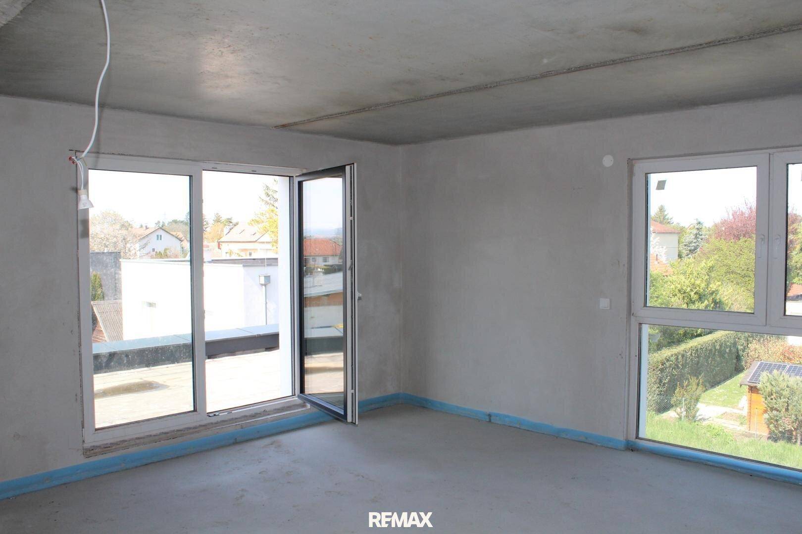 Rohbauzimmer mit großer Glastür, die Zugang zu einer potenziellen Dachterrasse bietet.