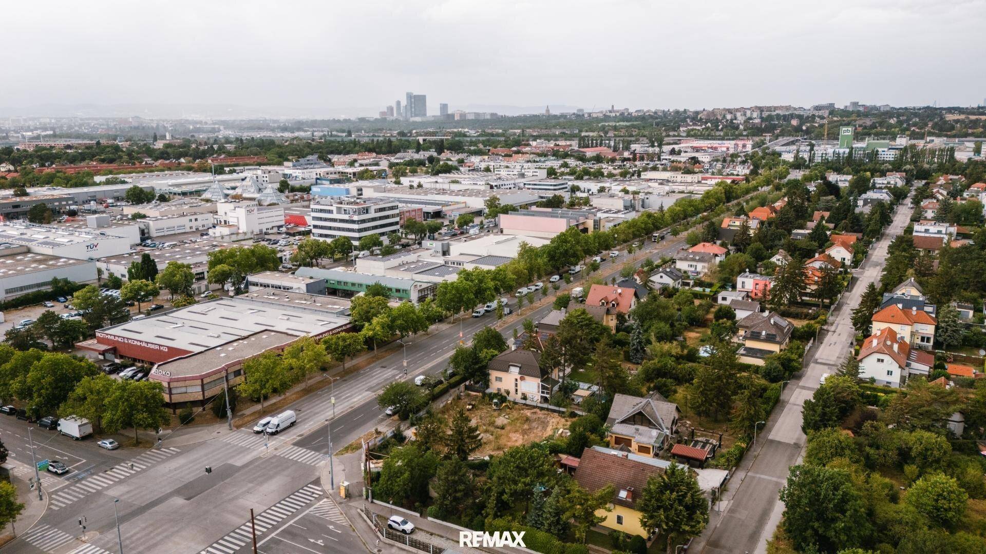 Panoramische Luftaufnahme einer Vorstadtlandschaft mit Wohngebieten, Gewerbeflächen und viel Grün.