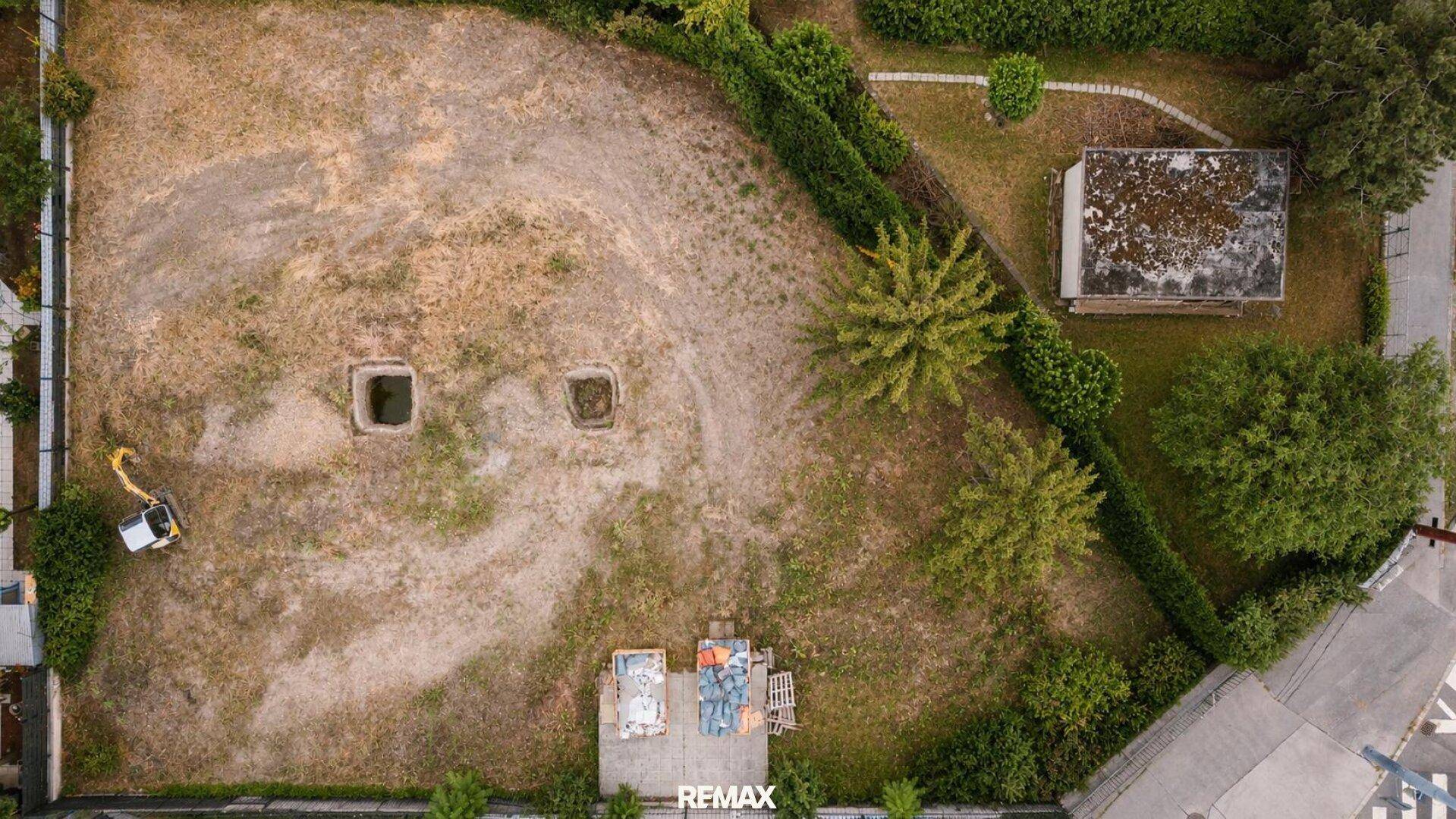 Senkrechte Luftaufnahme eines Grundstücks mit trockener Vegetation, umgeben von Hecken und Bäumen.