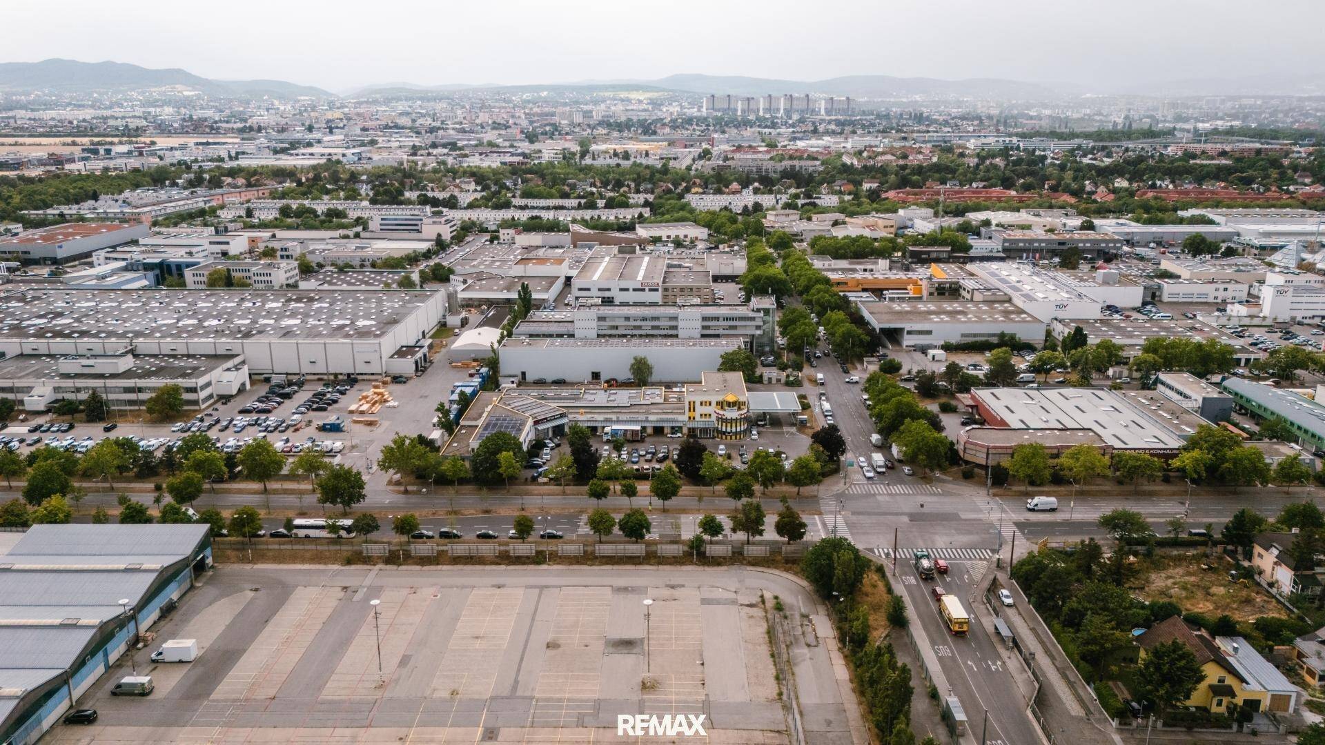 Luftaufnahme eines Gewerbegebiets mit großen Hallen und Parkplätzen, im Hintergrund Wohnsiedlungen.