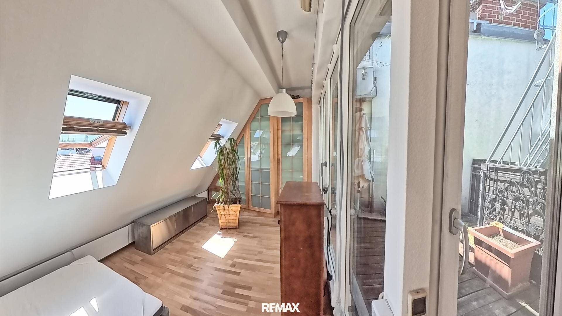 Gemütlicher Raum mit Dachschrägen, Holzboden und Zugang zu einem kleinen Balkon.