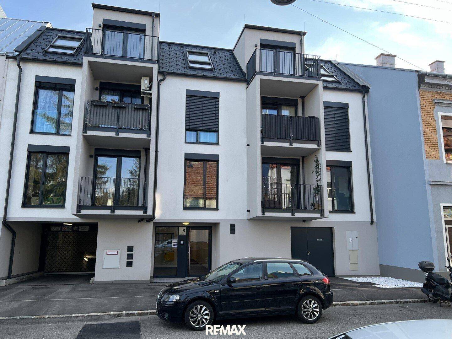 Ansicht der modernen Wohnhausfassade mit Balkonen und einem geparkten Auto davor.