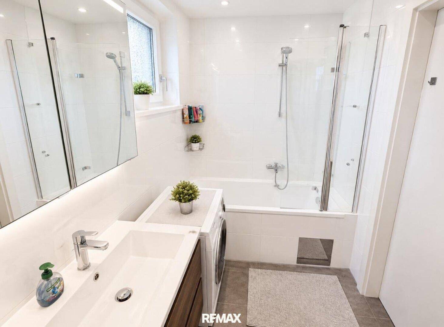 Helles Badezimmer mit Badewanne, Duschfunktion, Waschbecken und Waschmaschine.