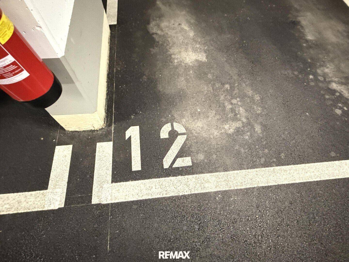Markierter Parkplatz Nummer 12 in einer Tiefgarage mit Feuerlöscher.