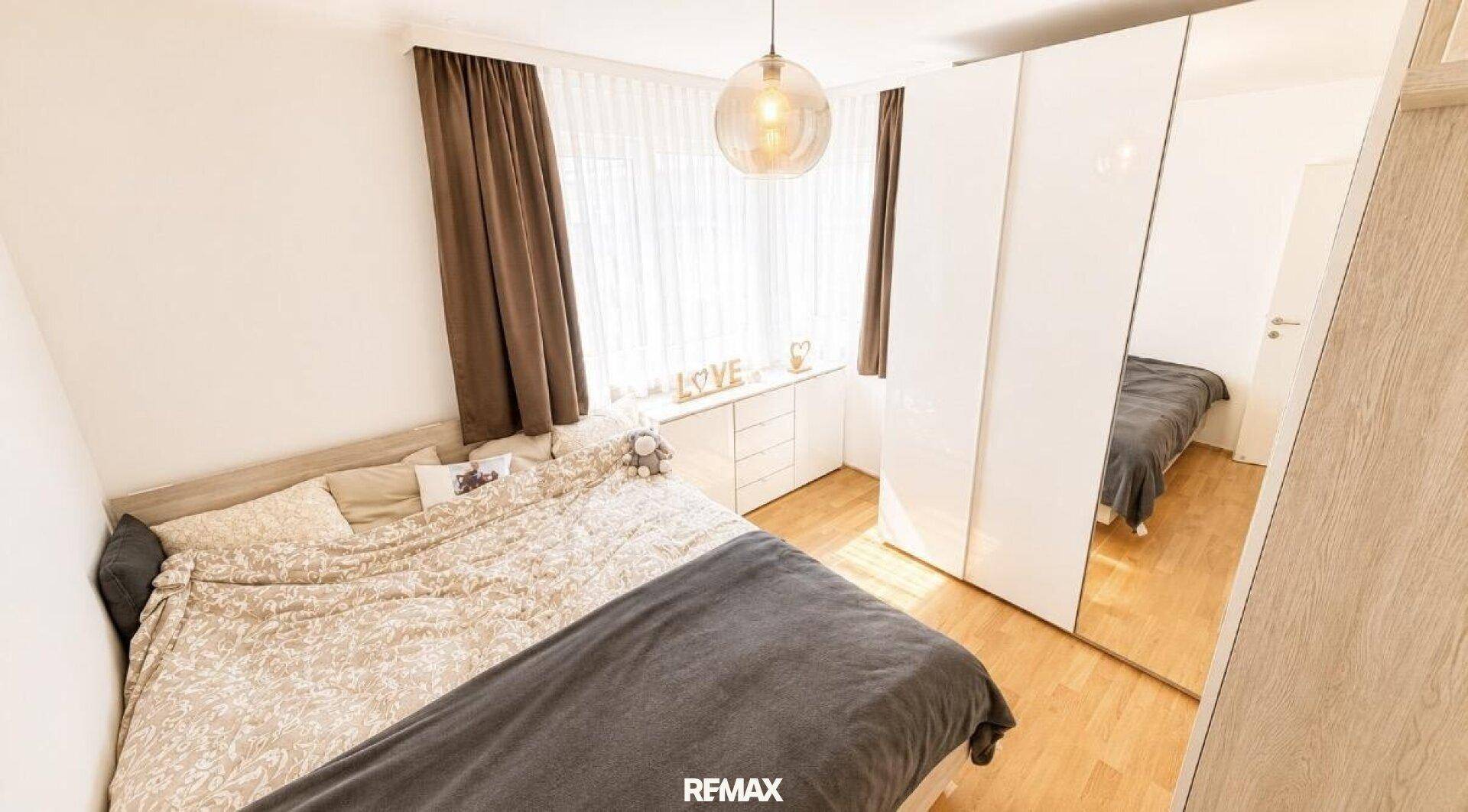 Helles Schlafzimmer mit Doppelbett, großem Spiegelschrank und Fenster für Tageslicht.