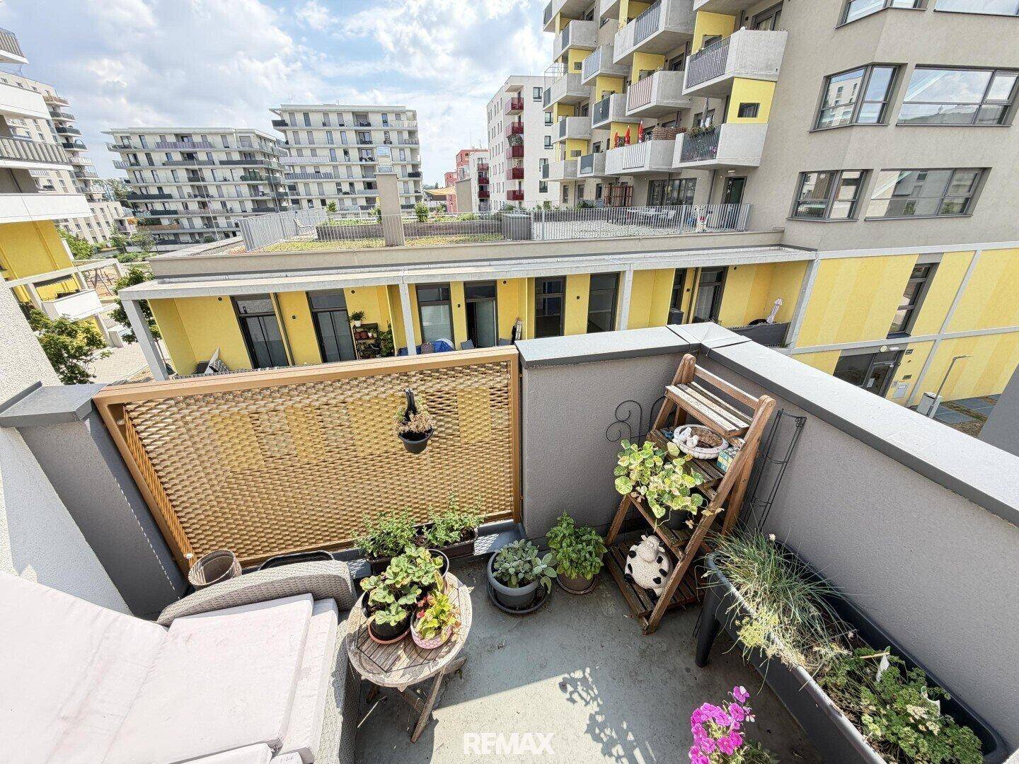 Kleiner, bepflanzter Balkon mit Sitzgelegenheit und Blick auf die umliegenden Gebäude.
