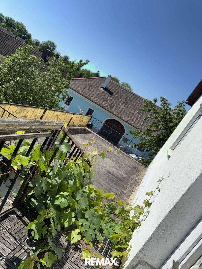 Blick von einem Balkon auf ein blaues Gebäude mit traditionellem Dach und üppiger Vegetation.