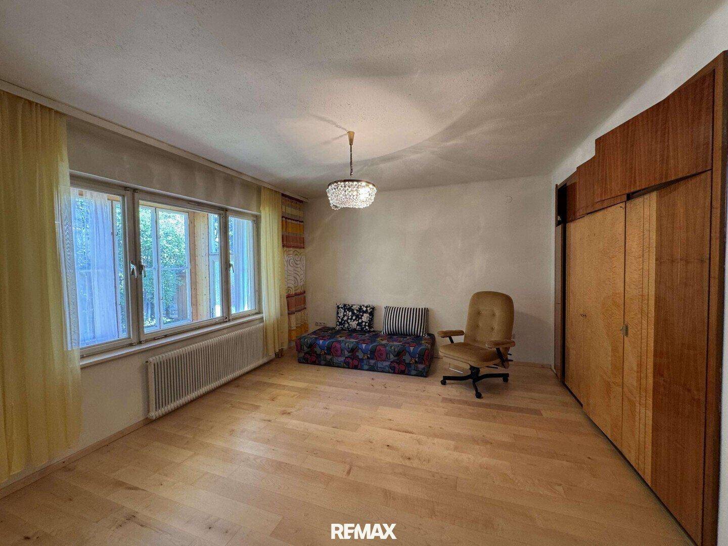 Helles Wohnzimmer mit Holzfußboden, großen Fenstern und einem Vintage-Kleiderschrank.