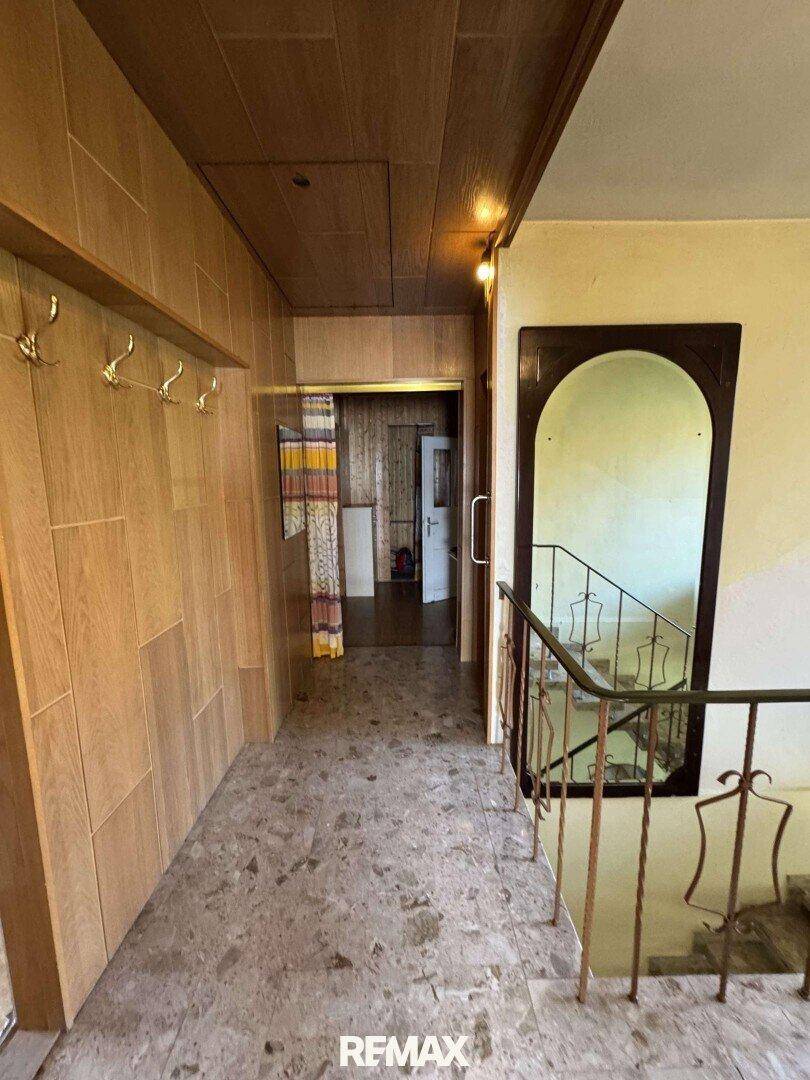 Flur mit Holzverkleidung, Terrazzoboden und einer Treppe mit schmiedeeisernem Geländer.