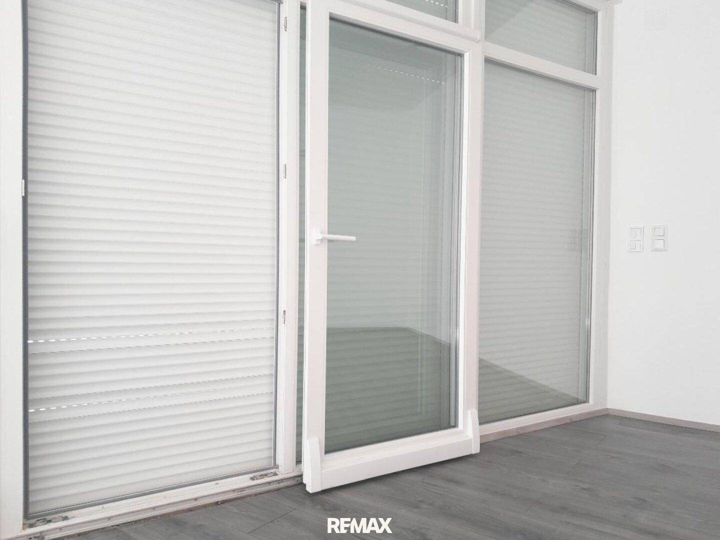 Große Fensterfront mit integrierten Jalousien und modernem grauen Laminatboden.