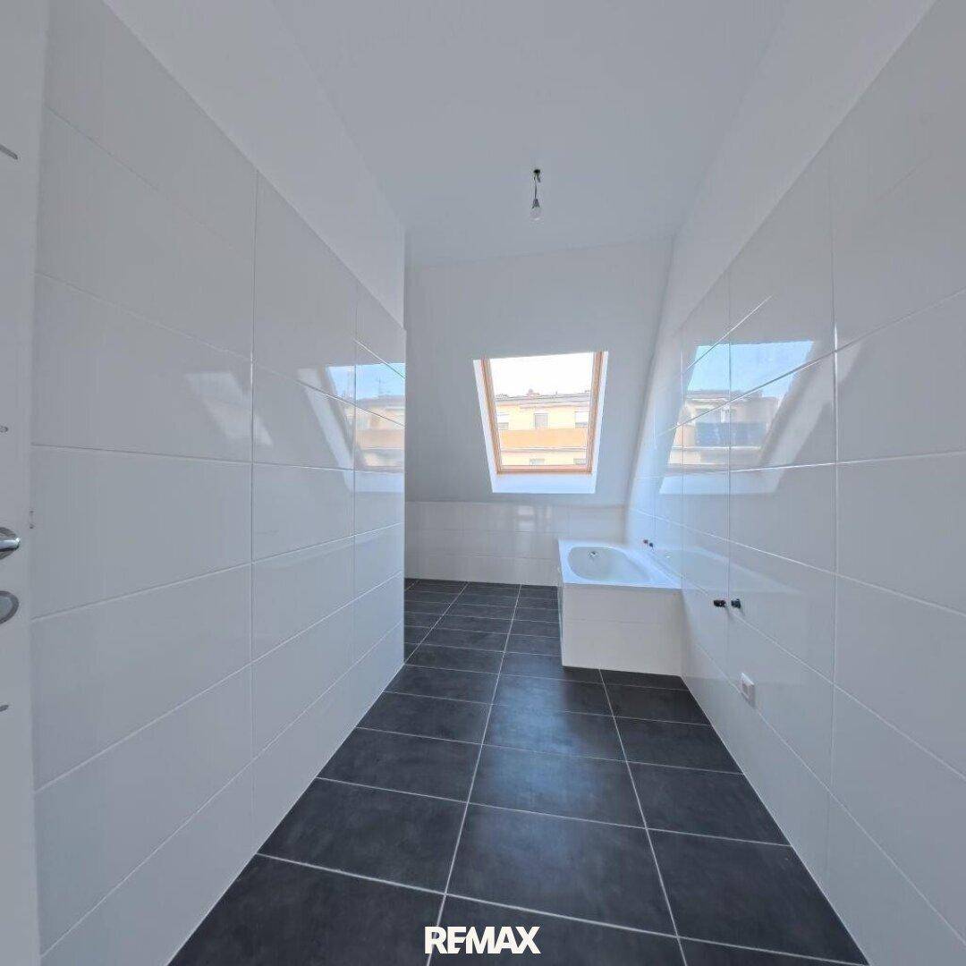 Modernes Badezimmer im Dachgeschoss mit Badewanne, Dachfenster und dunklen Fliesen.