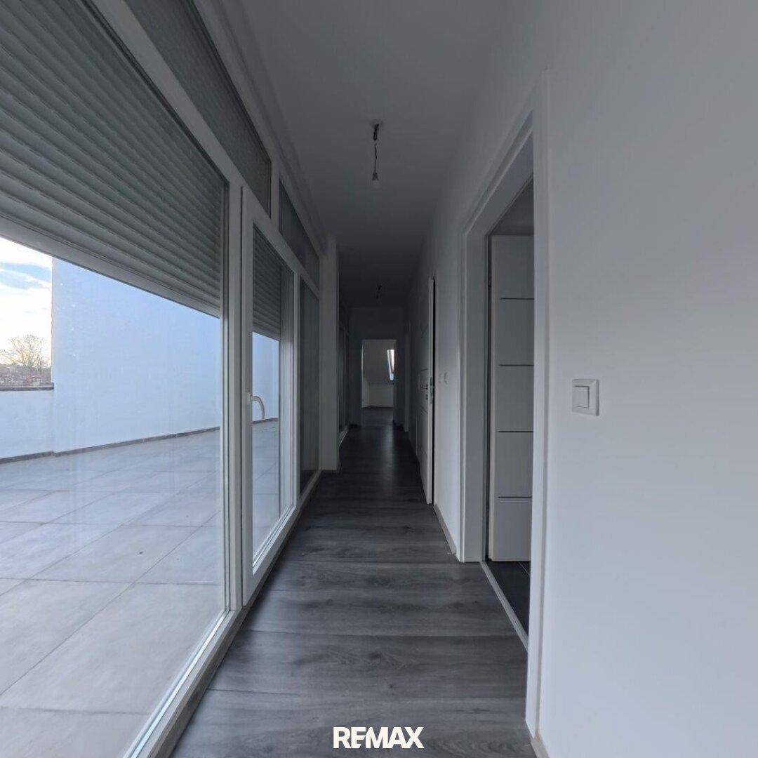 Langer, heller Flur mit grauem Laminatboden und Zugang zu einem Balkon oder einer Terrasse.