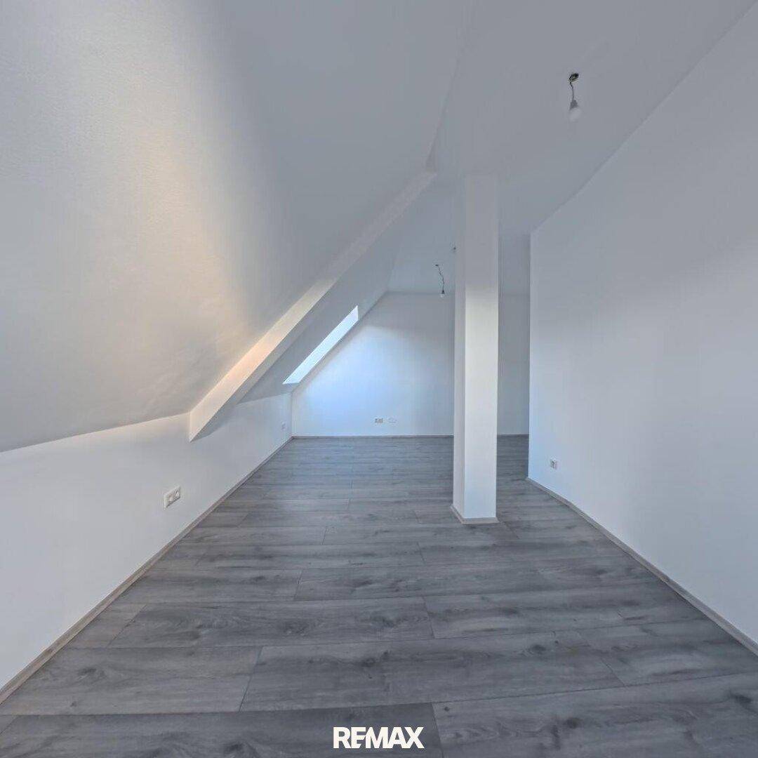 Helles Zimmer im Dachgeschoss mit Schrägdecke, Dachfenster und modernem Laminatboden.