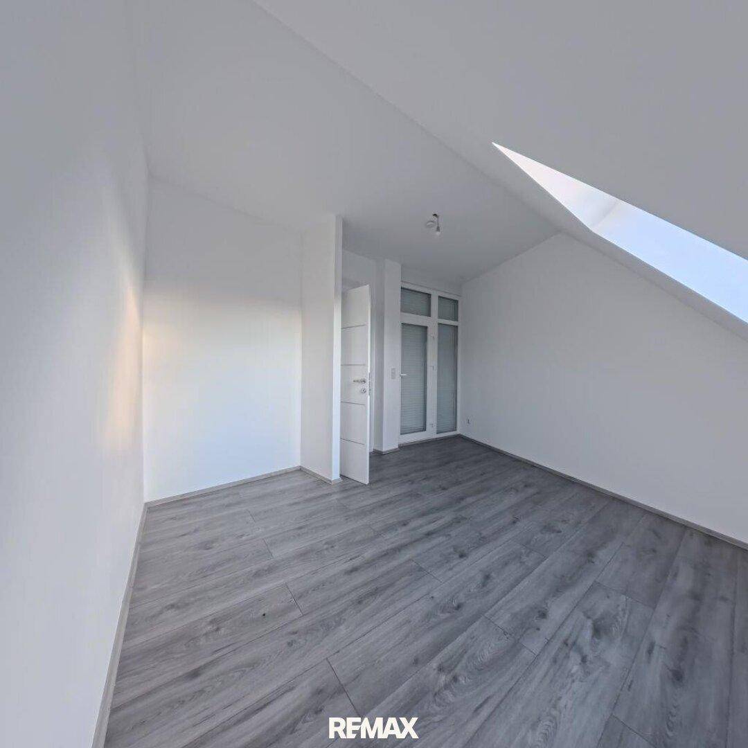 Geräumiges Zimmer im Dachgeschoss mit Schrägdecke und Zugang zu einem weiteren Bereich.