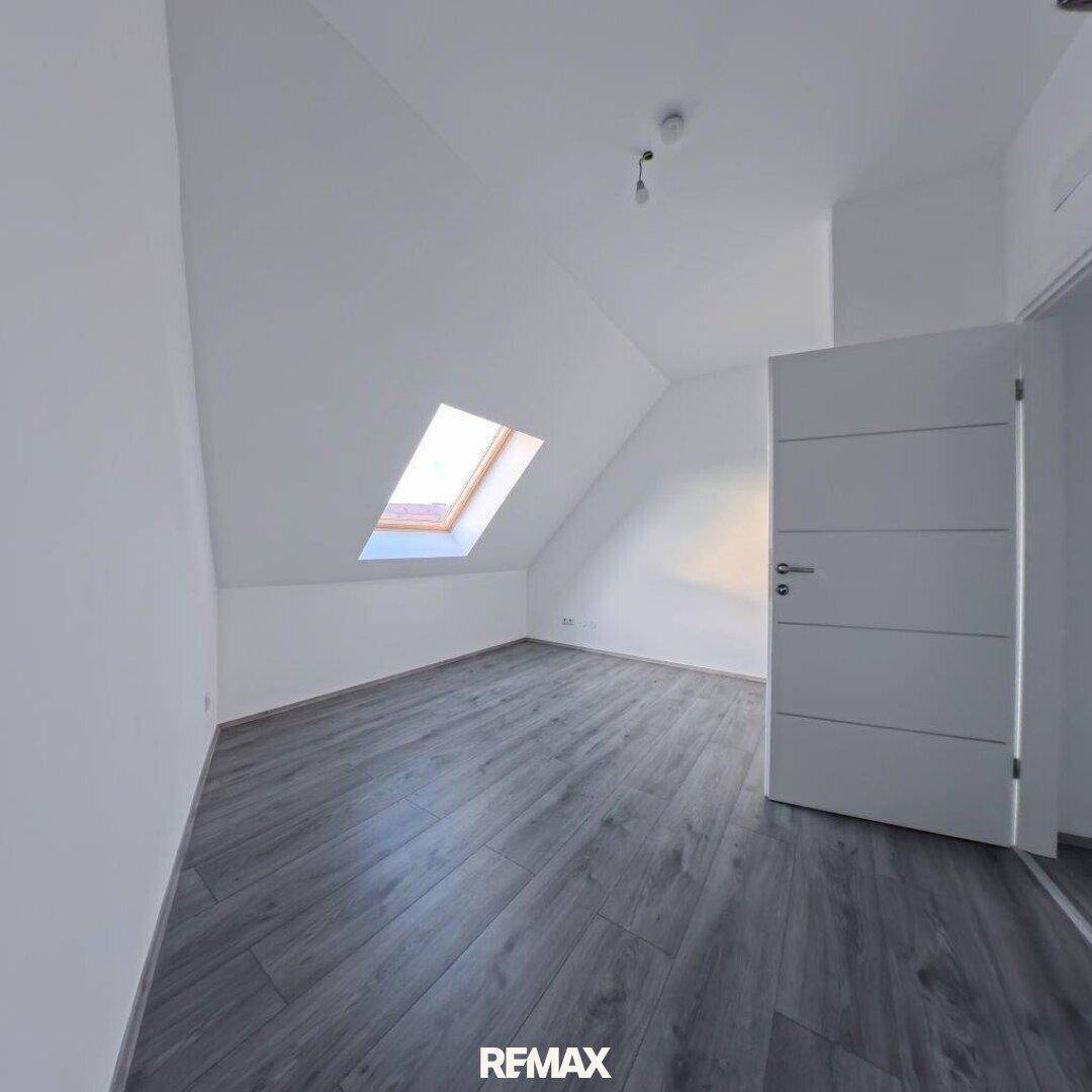 Helles Dachzimmer mit Schrägdecke, Dachfenster und modernem Laminatboden.