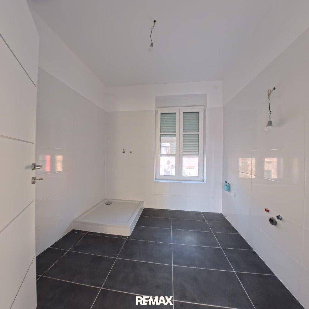 Modernes Badezimmer mit weißen Wandfliesen, dunklem Boden und vorbereiteter Duschwanne.