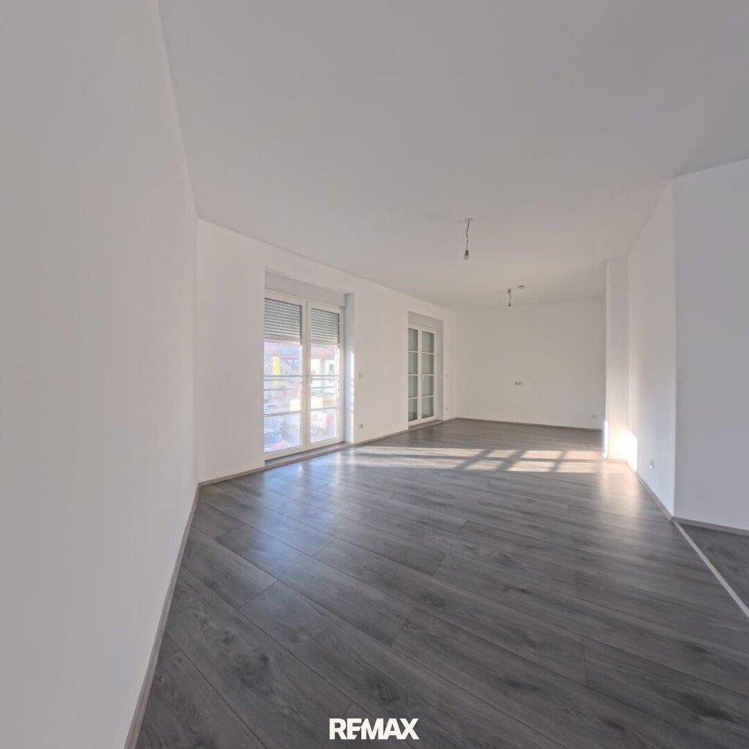 Geräumiger, heller Raum mit grauem Laminatboden und Fensterfronten mit Rollläden.