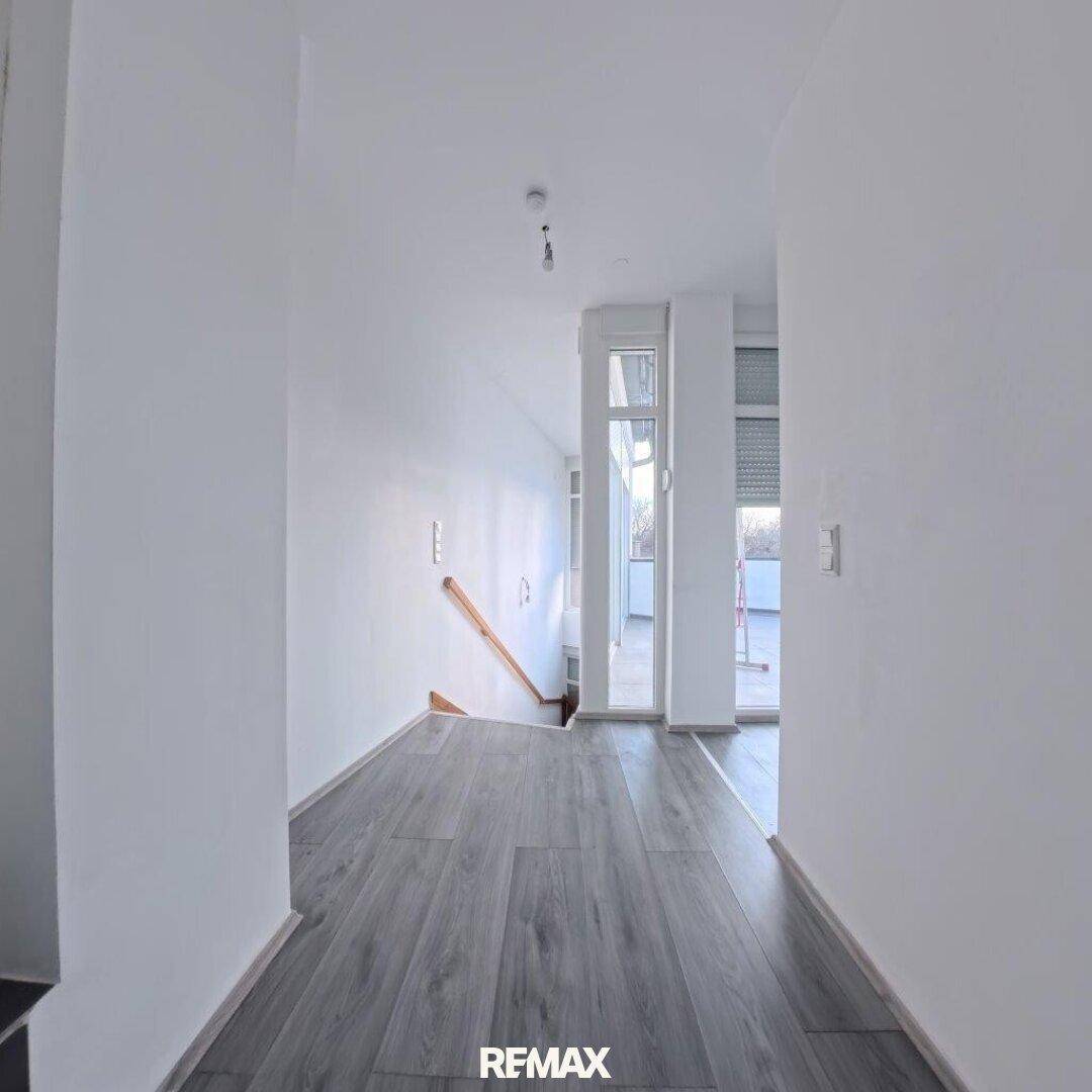 Heller Flur mit grauem Laminatboden, der zu weiteren Räumen und einer Treppe führt.