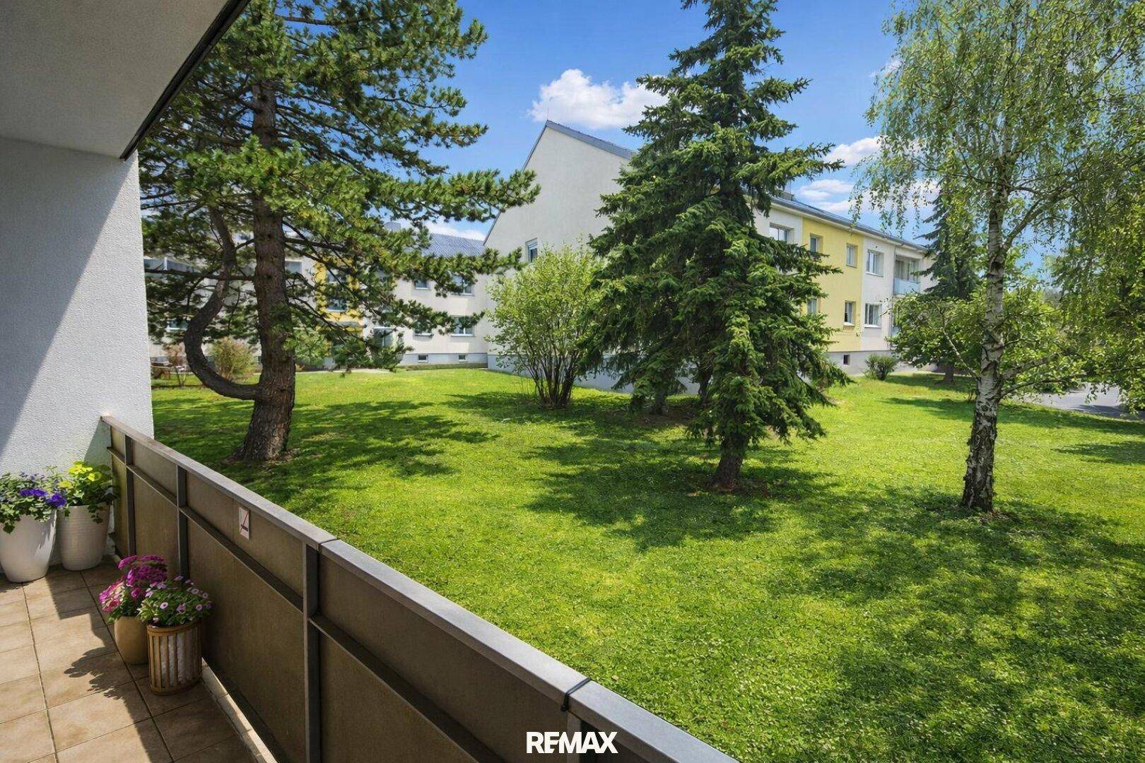 Balkon mit Blick auf einen gepflegten Gemeinschaftsgarten und umliegende Gebäude.