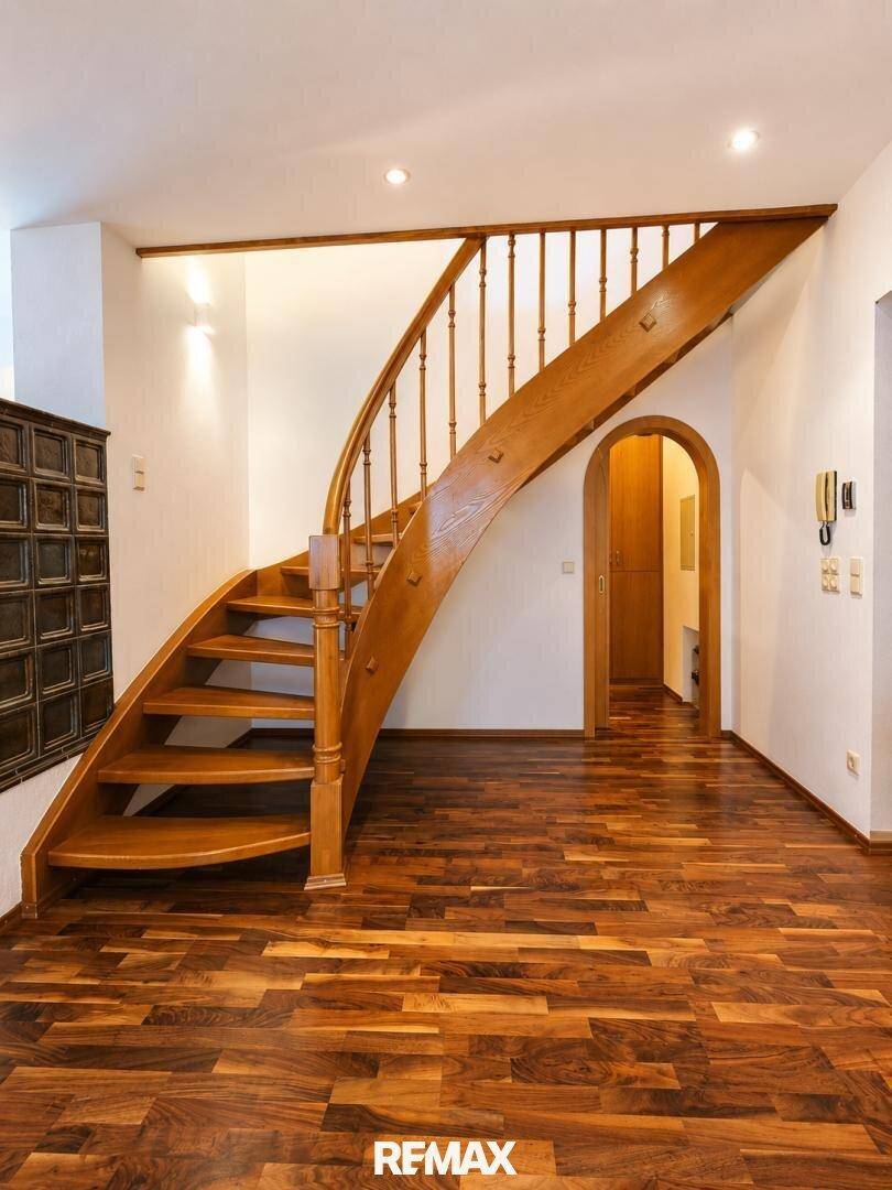 Elegante Holztreppe im Eingangsbereich mit dunklem Parkettboden und Kachelofen.