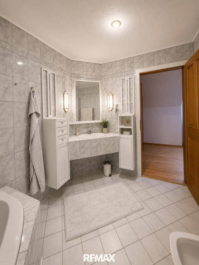 Gefliestes Badezimmer mit Einzelwaschbecken, Spiegelschrank und weißen Badmöbeln.