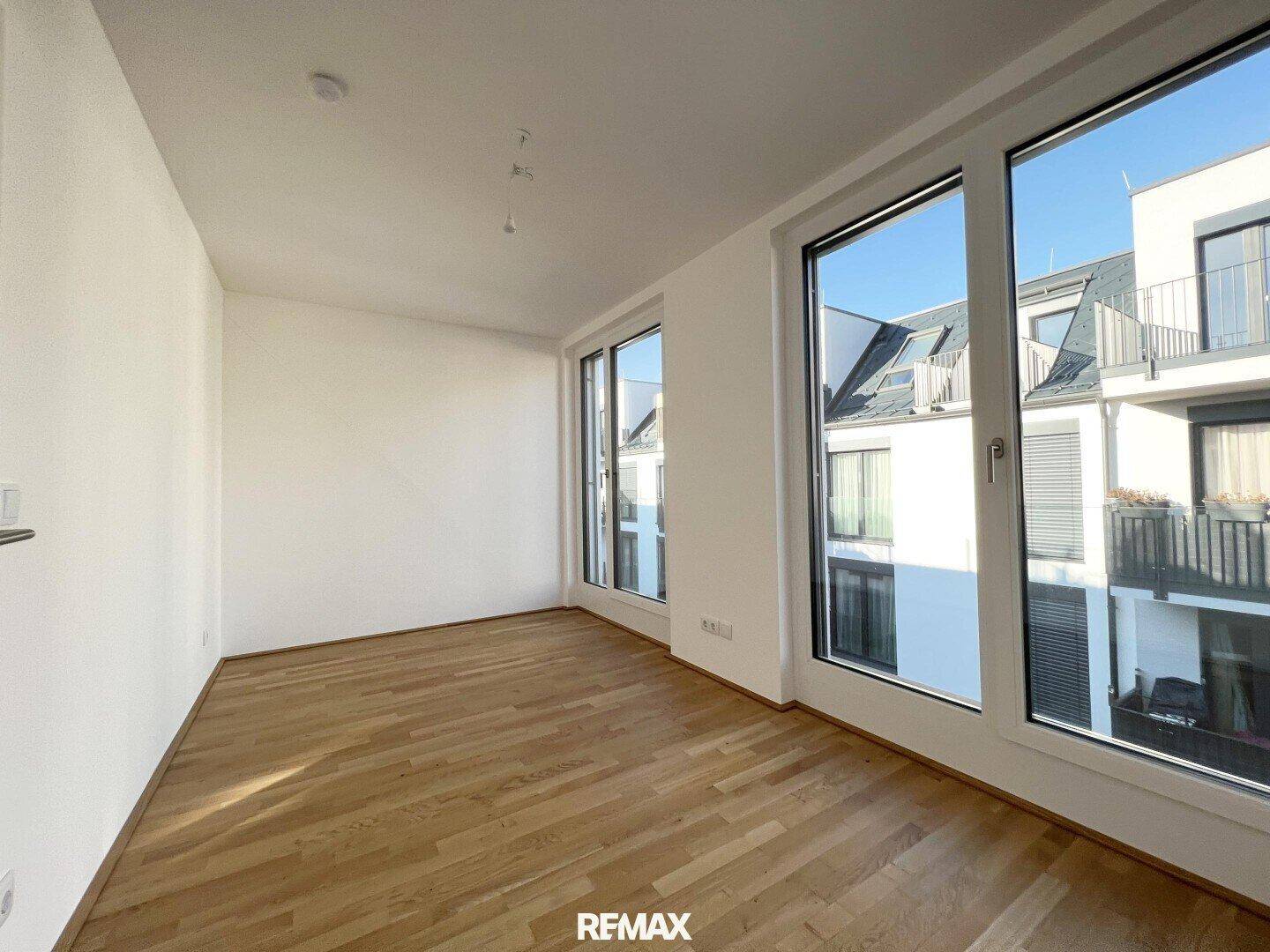 Helles, unmöbliertes Zimmer mit Holzboden und großen Fenstern, bietet vielseitige Nutzungsmöglichkeiten.