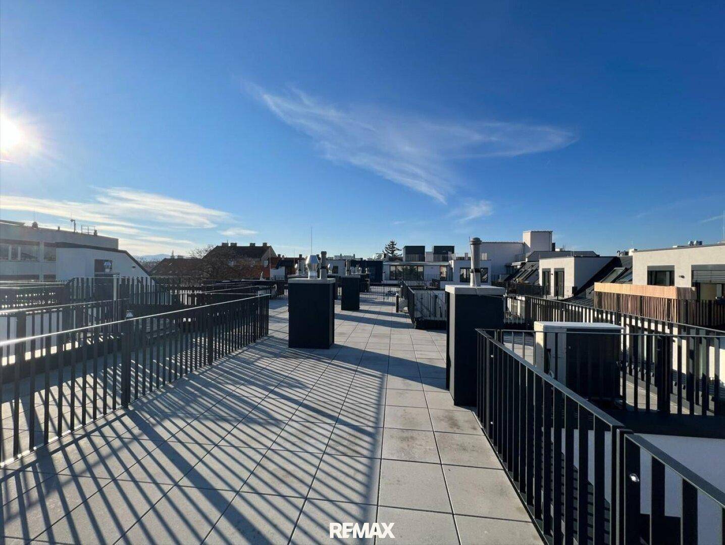 Weitläufige Dachfläche mit Fliesenboden und Geländer, bietet einen weiten Blick über die Dächer der Stadt.