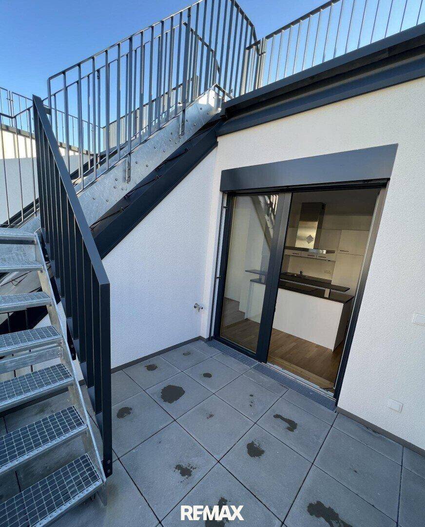 Unmöblierte Terrasse mit Fliesenboden und Treppe zur oberen Ebene, bietet direkten Zugang zum Innenbereich.