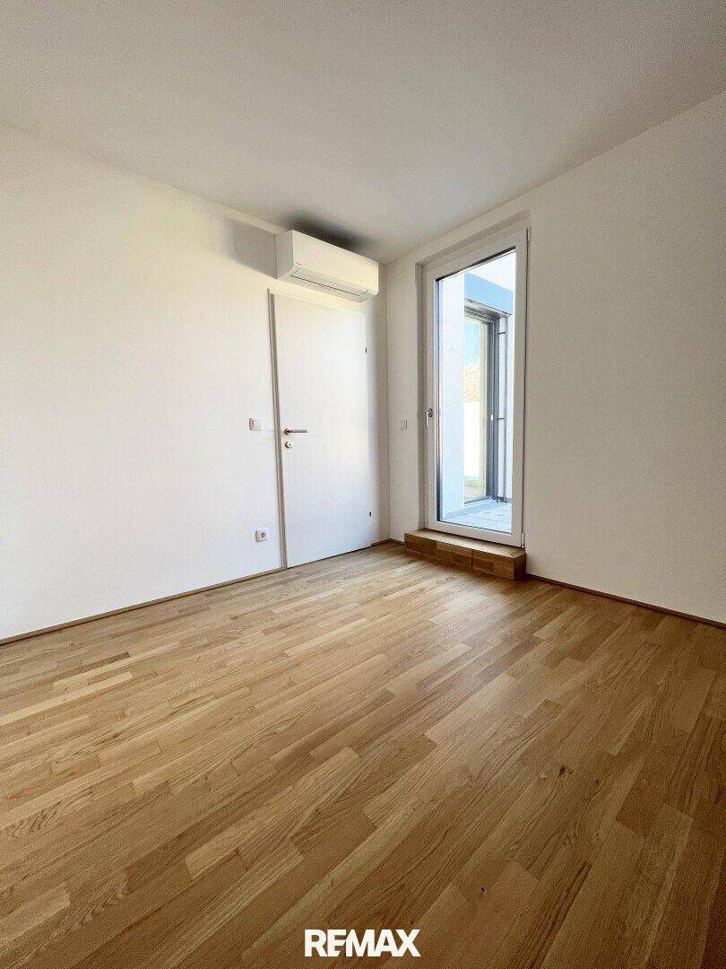 Unmöbliertes Schlafzimmer mit Holzboden, Klimaanlage und Zugang zu einem Balkon, bietet viel Gestaltungsfreiheit.