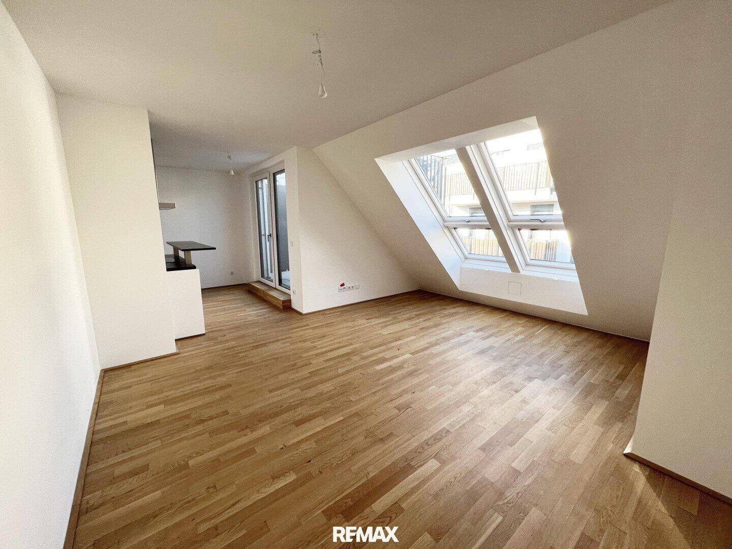 Geräumiges, unmöbliertes Wohnzimmer mit hellem Holzboden und großen Dachfenstern, ideal für individuelle Gestaltung.