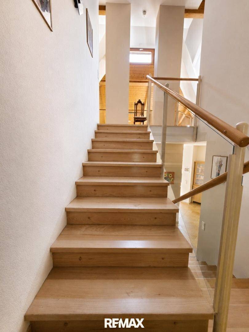 Helle Holztreppe mit Glasgeländer, die die verschiedenen Ebenen des Hauses verbindet.