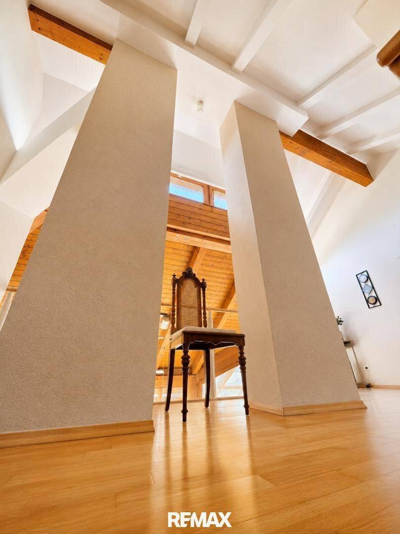 Hoher Flur im Obergeschoss mit Holzboden und einem dekorativen Stuhl.